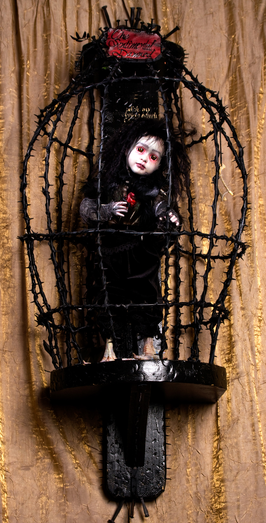 pale gothic red rimmed eyes black hair doll repaint black feathered velvet doll with taxidermied bird feet standing in a black thorn cage