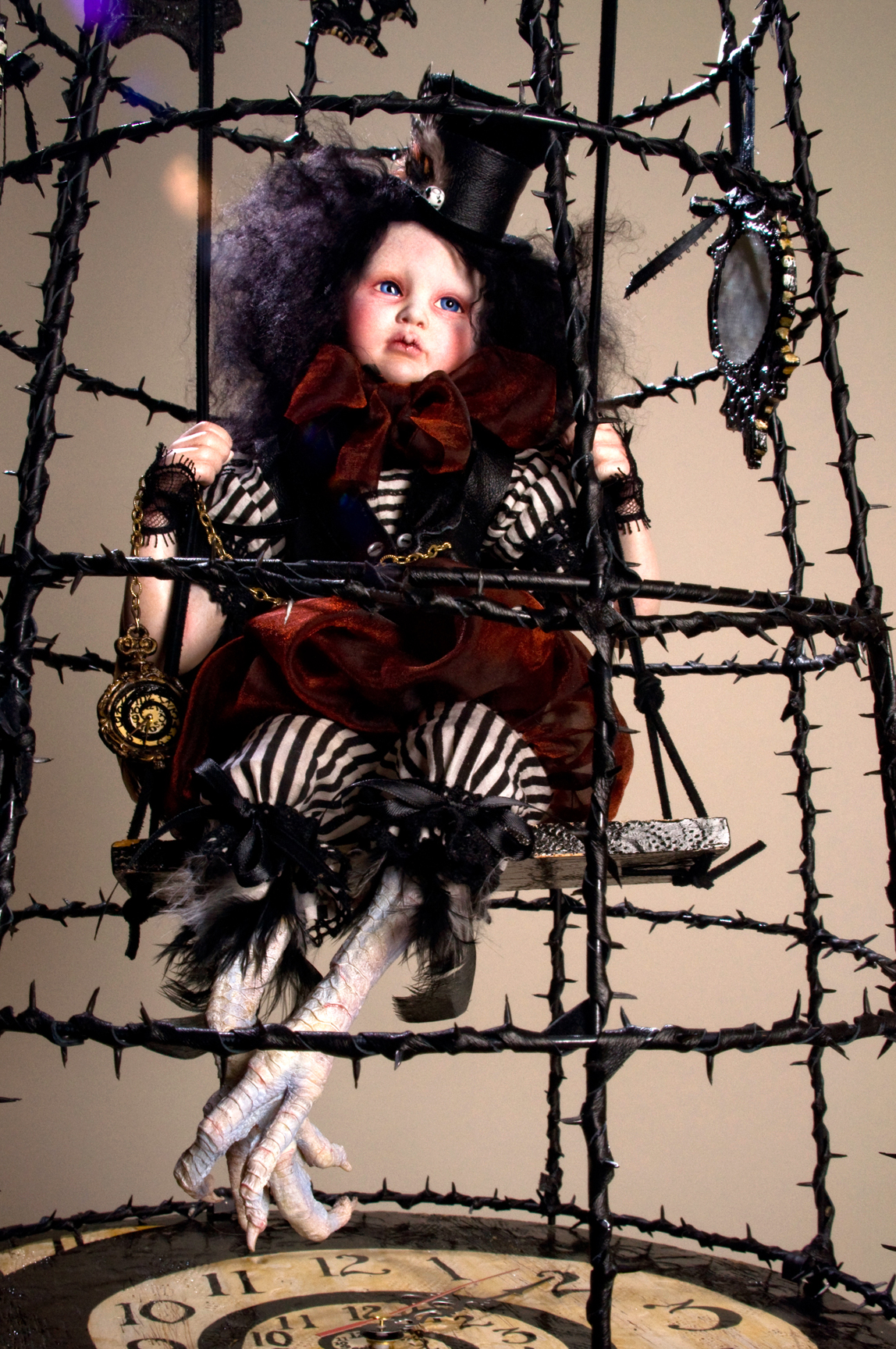 gothic artdoll wearing black tophat with black hair taxidermied bird feet suspended in a cage with a hand-painted clock spiral base in a thorny black birdcage surrounded by gothic portraits of himself