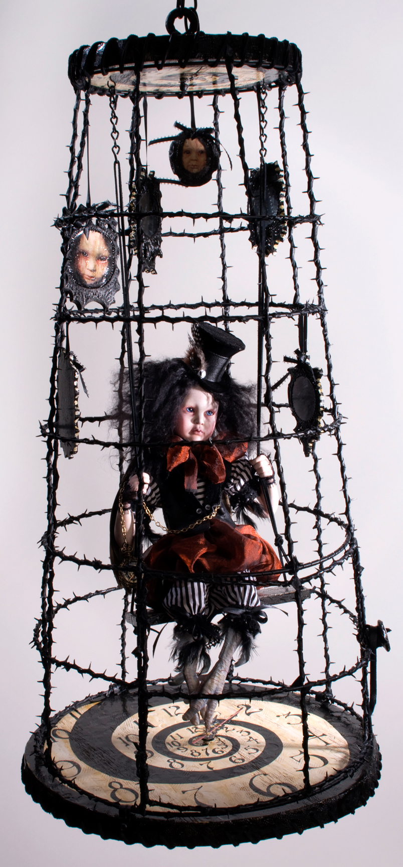 gothic artdoll wearing black tophat with black hair taxidermied bird feet suspended in a cage with a hand-painted clock spiral base in a thorny black birdcage surrounded by gothic portraits of himself