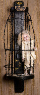 blond feathered pale gothic artdoll wearing white lace with taxidermied bird feet in a black thorn cage with a tiny secret door