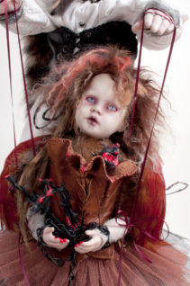 close-up of the fool doll gothic feathered artdoll with leather vest chained hands and blood