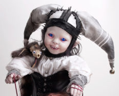 close up sinister gothic jester art doll wearing jester cap with bells black spiked leather and black leather corset