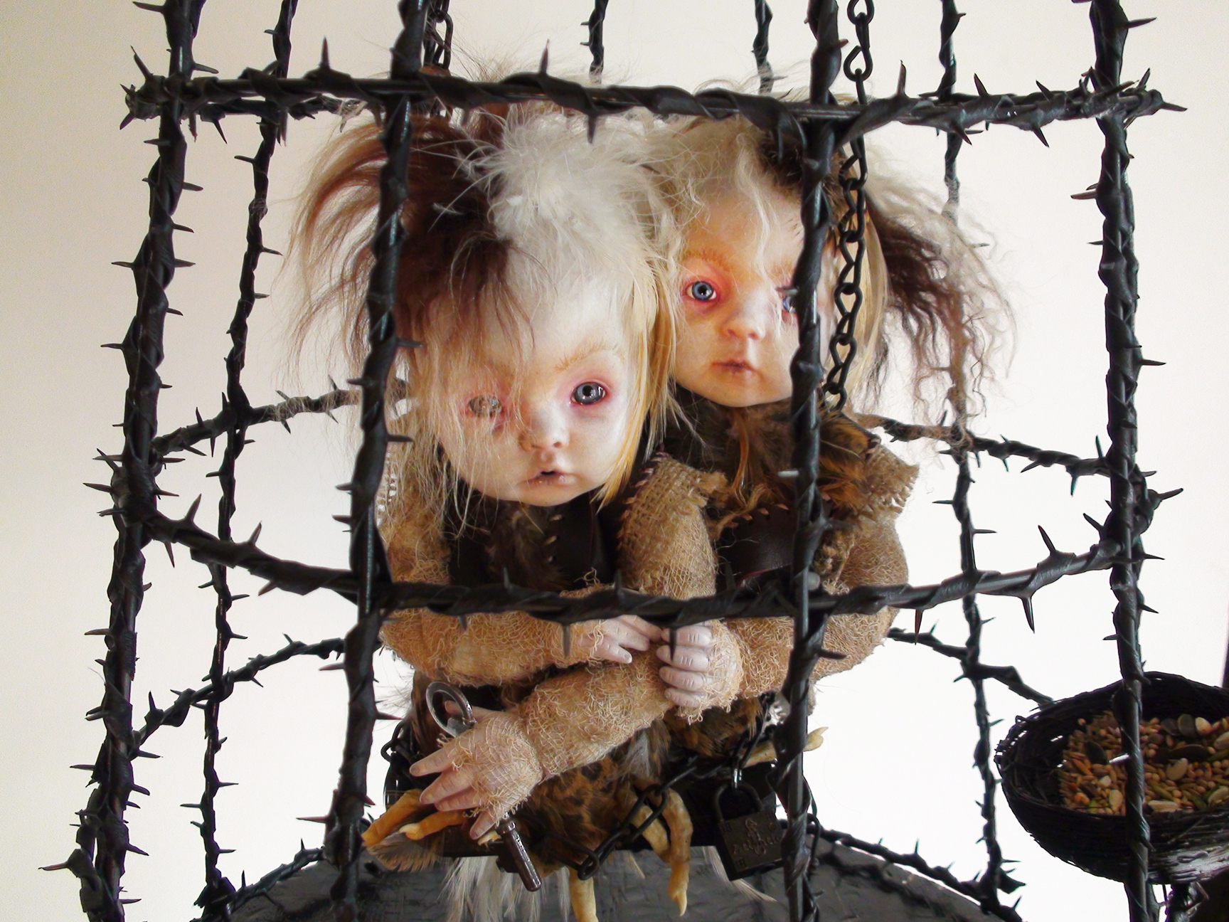a pair of gothic feathered art dolls huddled together on a perch inside a black thorned cage mixed media assemblage art piece