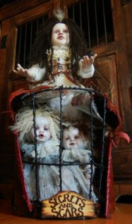 large gothic artdoll with a black thorn cage with two ghostly white smaller porcelain dolls held in the cage