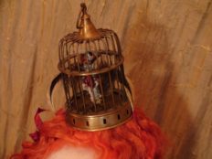close-up of brass bird cage hat with sculpted bird inside