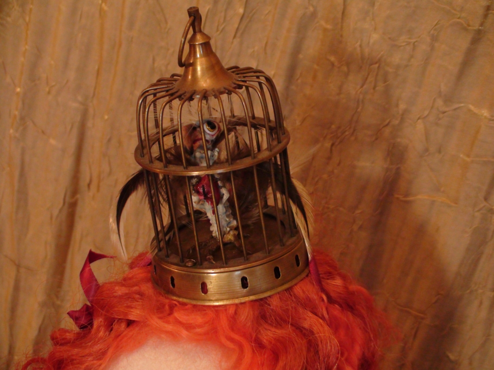 close-up of brass bird cage hat with sculpted bird inside