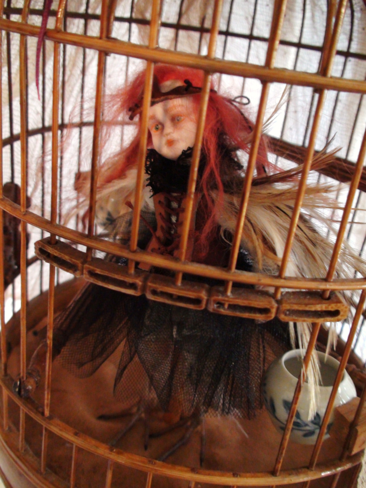 close-up detail of a bird artdoll with red hair and brown feathers in a brass birdcage