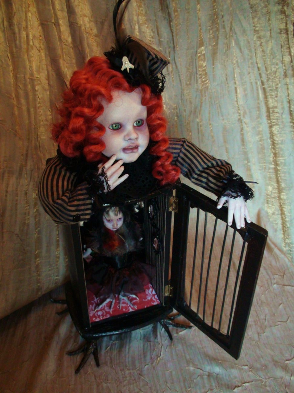 gothic redhead artdoll wearing stripes with cage cabinet body holds a miniature feathered porcelain doll with taxidermy birdfeet.