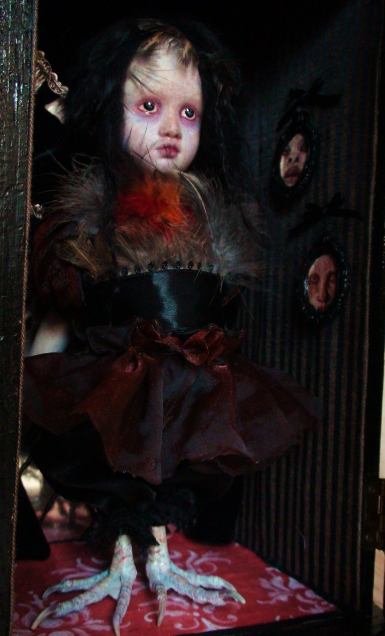close-up miniature porcelain artdoll gothic repaint with black hair wearing feathers and dark red maroon skirt, taxidermy birdfeet standing in cabinet with striped wallpaper