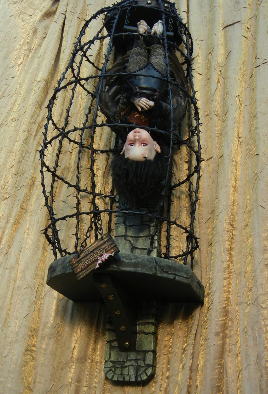 wall-mounted cage holding an upside-down black feathered gothic artdoll