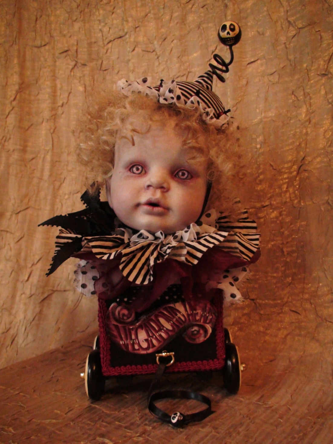 gothic dark circus travelling golden curled baby head wearing striped ruffled collar on a hand-painted pull-cart toy music box