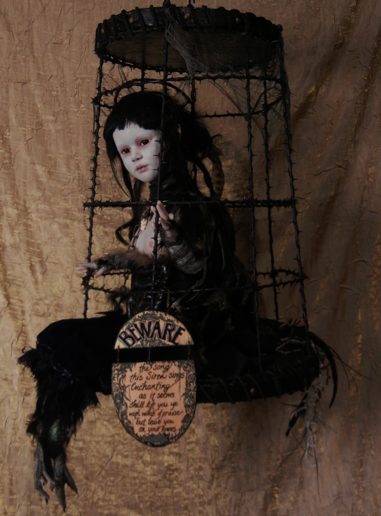 taxidermy artdoll mixed media assemblage of a pale goth doll with black feathered bird feet sitting in a suspended black cage