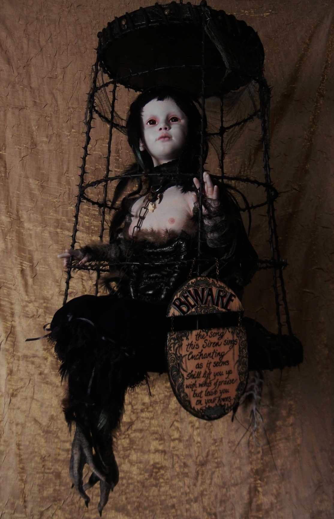 taxidermy artdoll mixed media assemblage of a pale goth doll with black feathered bird feet sitting in a suspended black cage