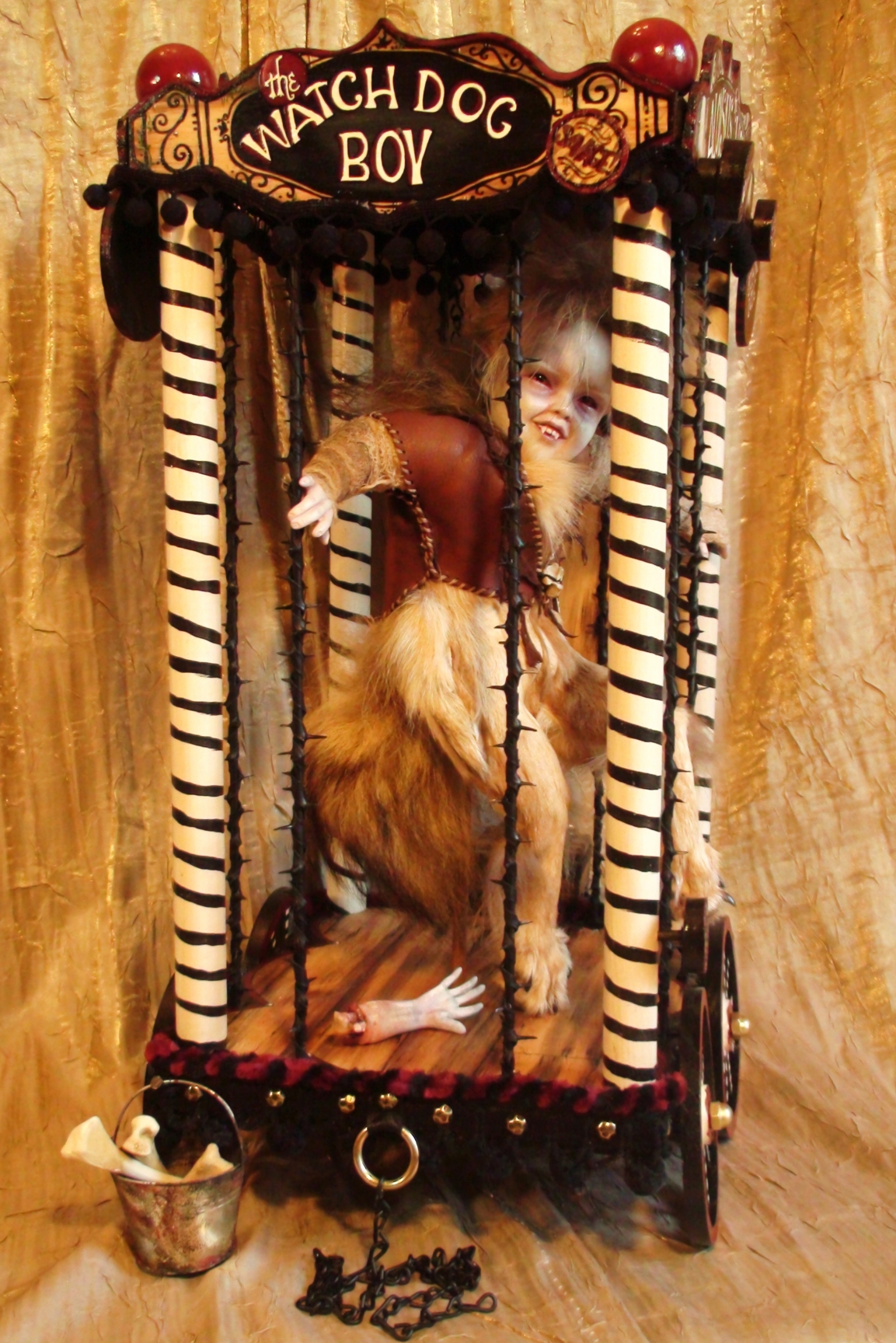 side view artdoll of a watchdog boy wolf boy sideshow attraction taxidermy assemblage in a cage carnival cart pull toy with hand painted signs and wheels bucket of bones