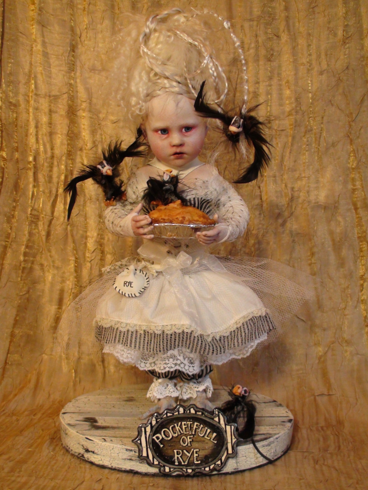 gothic artdoll pale with blond braids and blue eyes wearing white dress black birds flying around her out of pie she holds