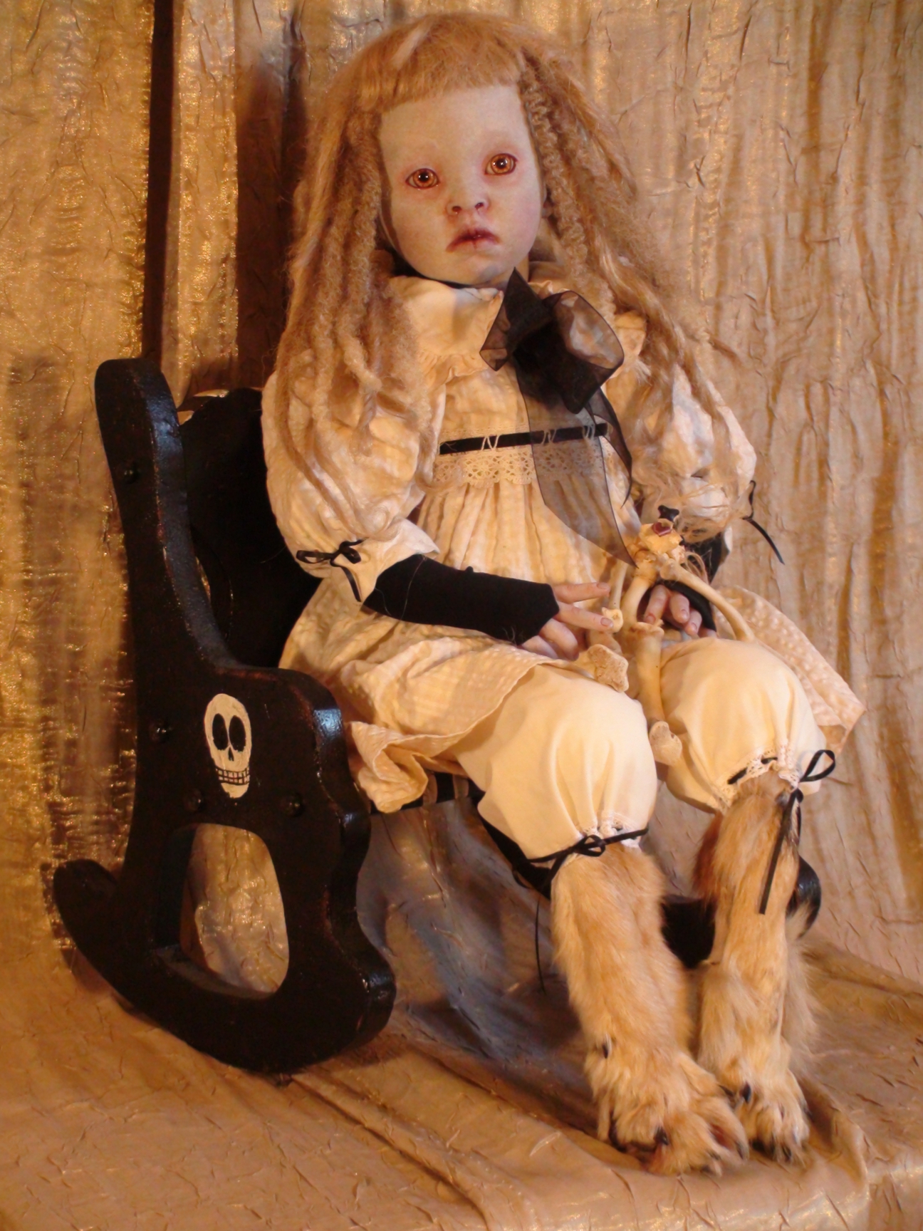 gothic fantasy artdoll with taxidermy stuffed coyote legs she is pale with orange eyes and blond hair dredlocks she wears a tea-stained dress and sits with a bone dog toy in her lap