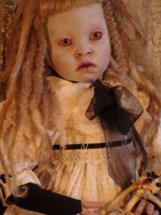 close-up of gothic fantasy artdoll she is pale with orange eyes and blond hair dredlocks she wears a tea-stained dress and sits with a bone dog toy in her lap