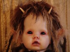 close-up of gothic doll face repainted porcelain pale with black eyes, short brown hair and horns