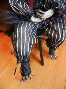 close-up detail taxidermy raccoon paw feet peeking out of black and white striped doll clothes