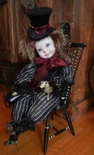 mixed media artdoll porcelain doll brown hair, repainted face wears top hat and black and white striped suit, red ribbon, taxidermied raccoon paws sitting painted black chair