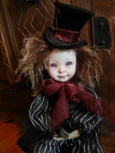 mixed media artdoll porcelain doll brown hair, repainted face wears top hat and black and white striped suit, red ribbon, taxidermied raccoon paws sitting