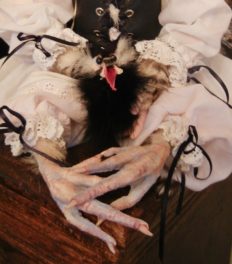 close-up detail doll's taxidermy chicken feet wearing white doll clothes with a feathered pet creature in his lap