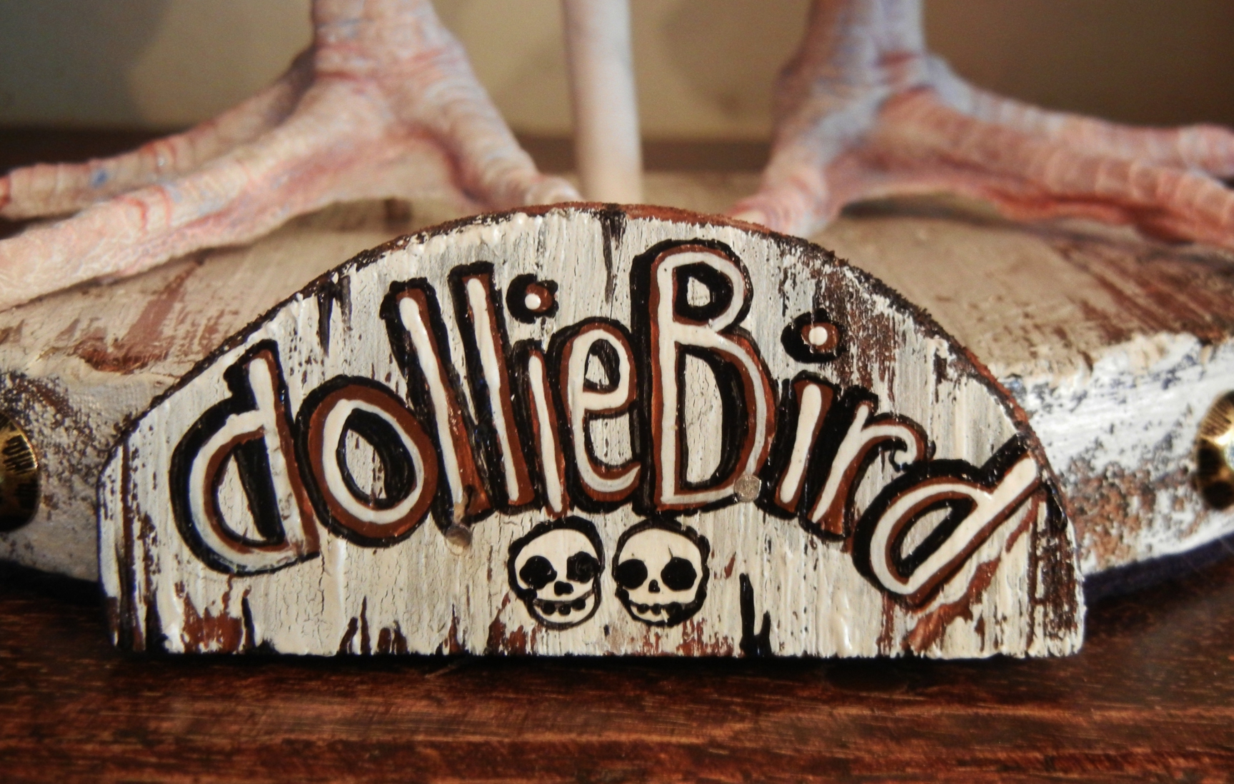 hand painted lettered wooden sign reads DollieBird with two tiny skulls