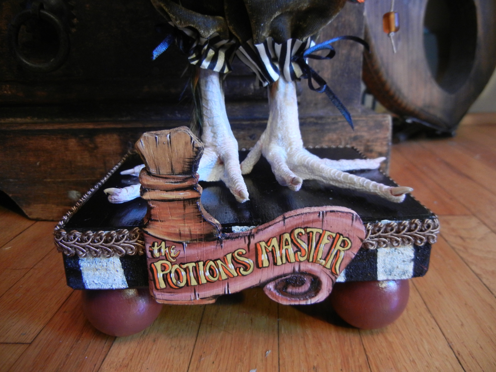 close-up detail taxidermy bird feet on painted black and white stripe wood platform with hand-painted lettered sign reading the Potions Master