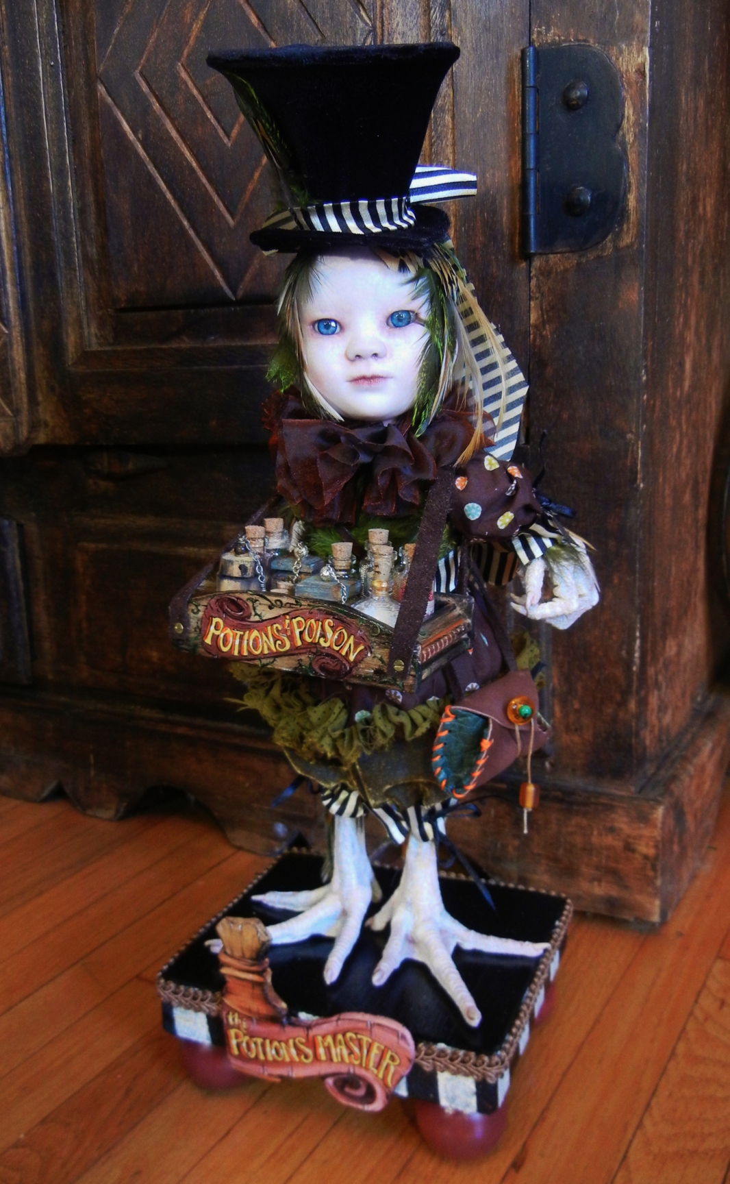 mixed media gothic artdoll green-feathered porcelain doll wearing black velvet tophat has taxidermy birdfeet and holds wooden tray of assorted glass bottles of potions and poisons
