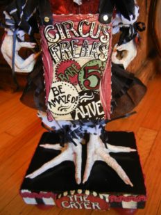 close-up circus-themed sideshow hand painted sign board reads Circus Freaks doll with taxidermy birdfeet standing on hand-painted wooden platform