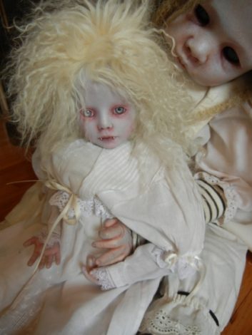 a gothic art doll holds a smaller doll in her lap they're both dressed in white nightgowns