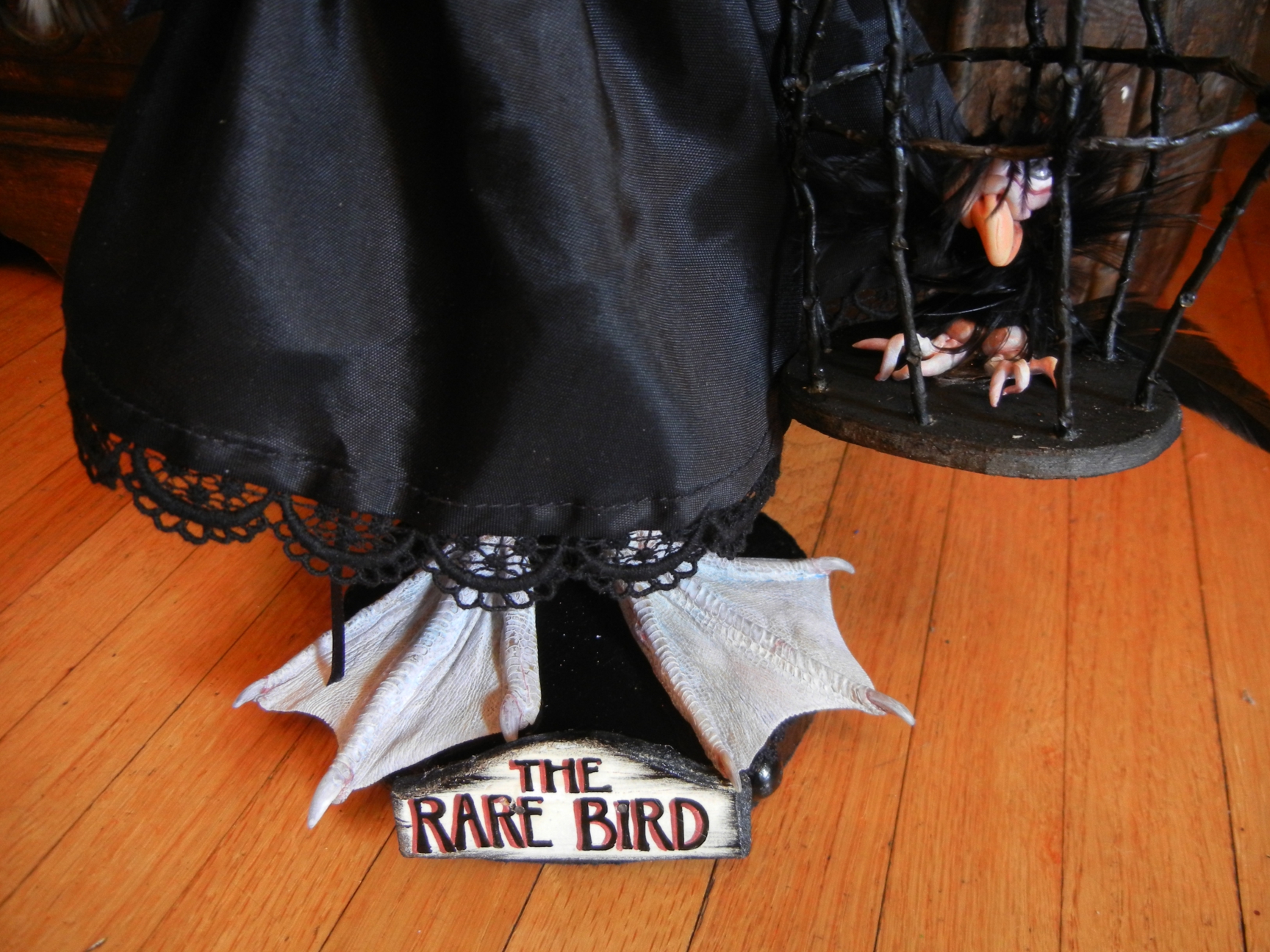 doll with taxidermy webbed bird feet standing on a wooden platform with a handpainted sign that says The Rare Bird