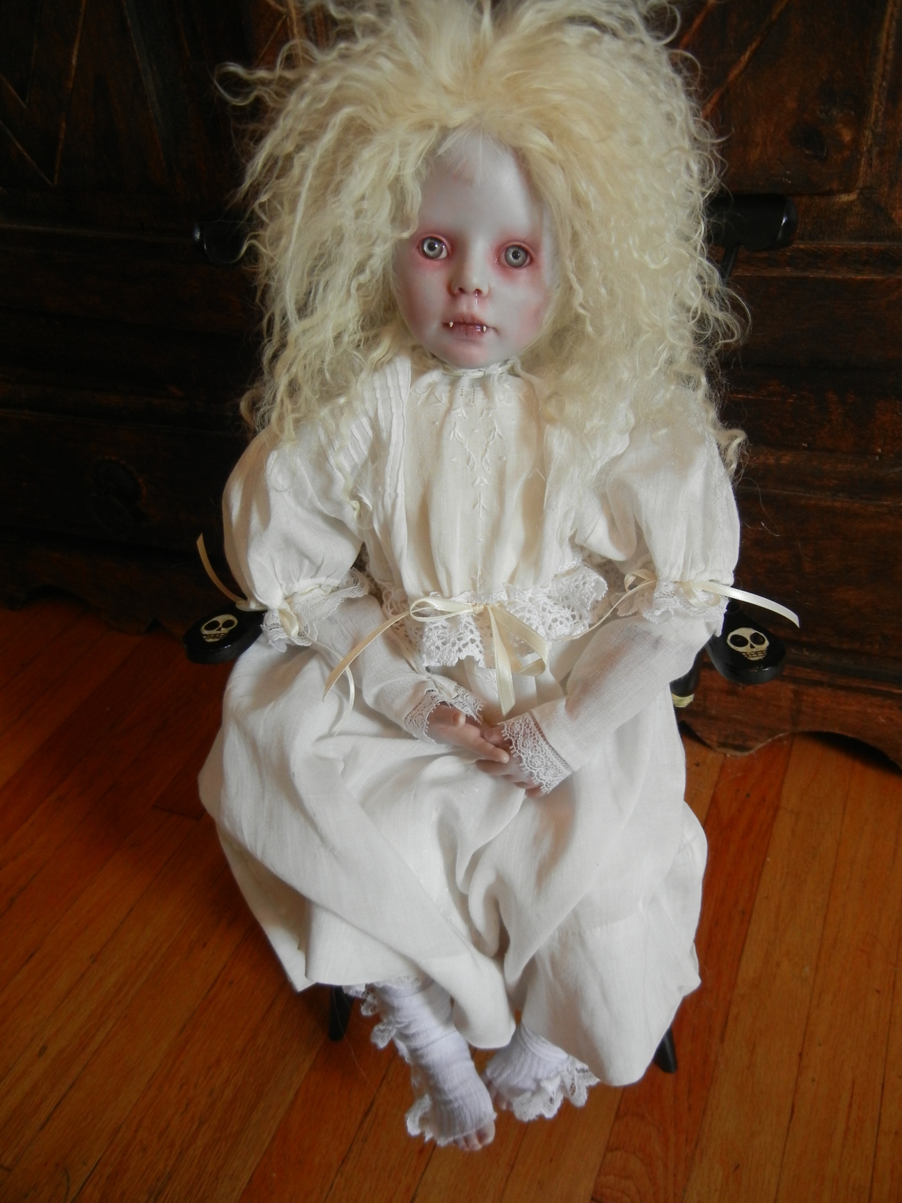 seated gothic vampire artdoll with white blond hair and fangs in a white nightgown