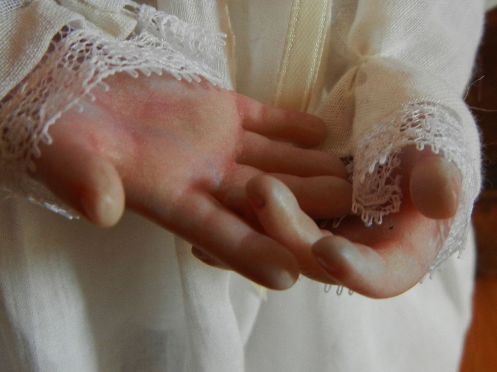 close up of painted doll hands white nightgown with lace cuffs