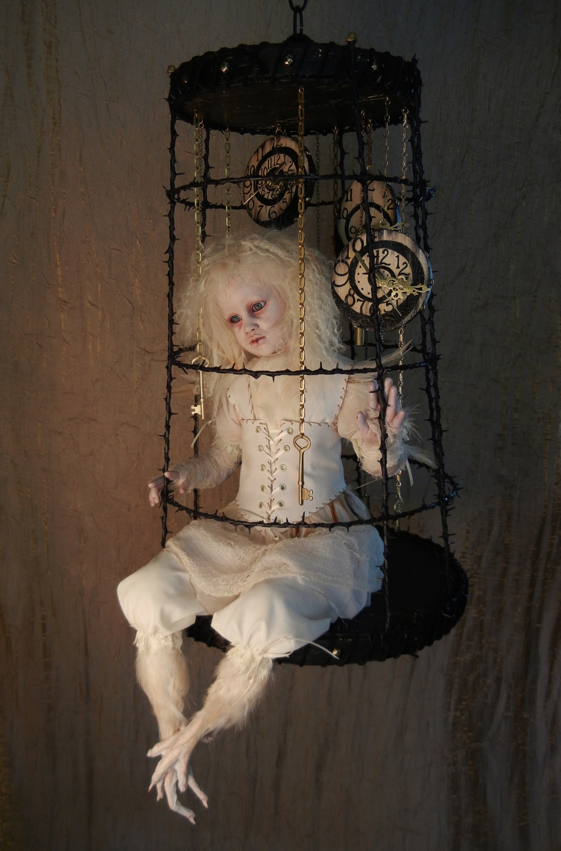 taxidermy artdoll assemblage of a white thornbird doll with feathered feet sitting in a suspended cage surrounded by hand painted clocks