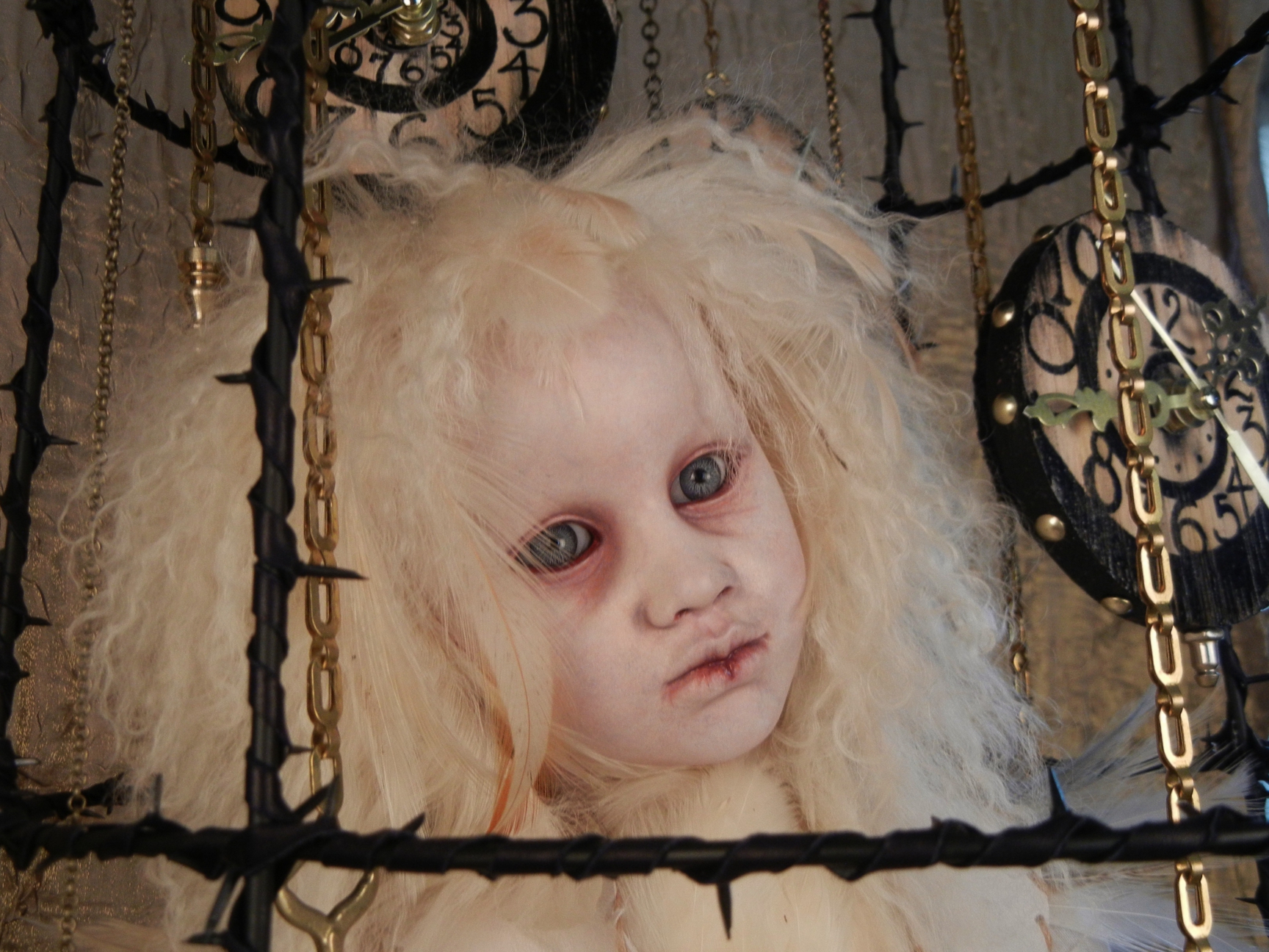close-up of taxidermy artdoll assemblage of a white thornbird doll sitting in a suspended cage surrounded by hand painted clocks and hanging gold keys