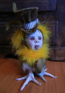 porcelain babydoll head with tongue sticking out, brown top hat, yellow and brown feathered bird body with taxidermy birdfeet