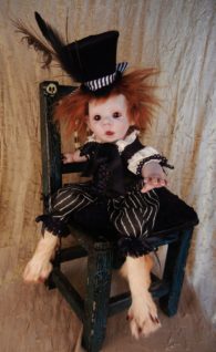 mixed media artdoll porcelain doll red hair, repainted face wears feathered top hat and bloomers taxidermied feet sitting in painted green chair