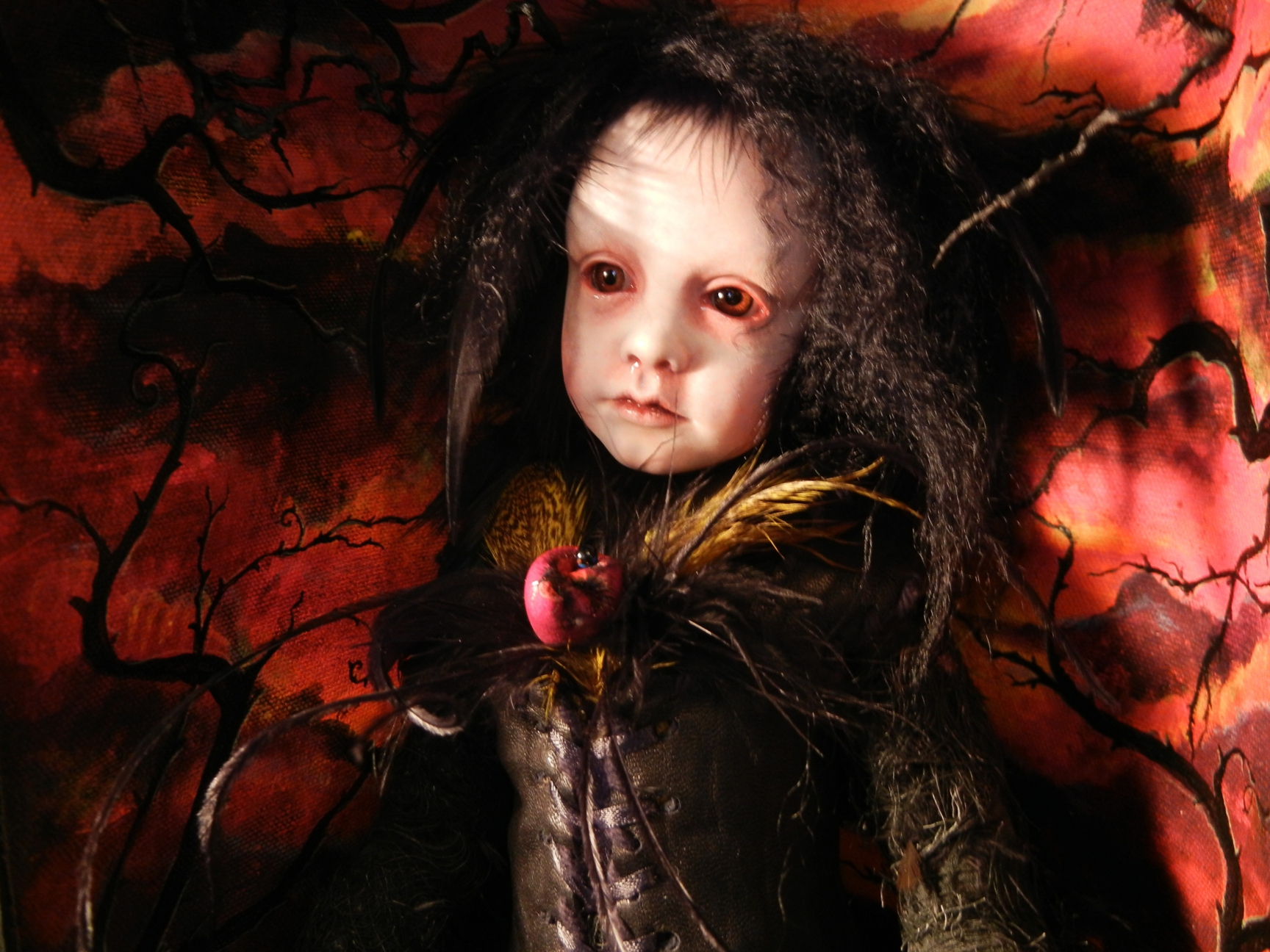 miniature goth doll pale with black hair and black clothes in front of red background black branches