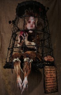 mixed media assemblage taxidermy art doll sorrowful doll dressed in velvet sits in cage with feathered bird feet