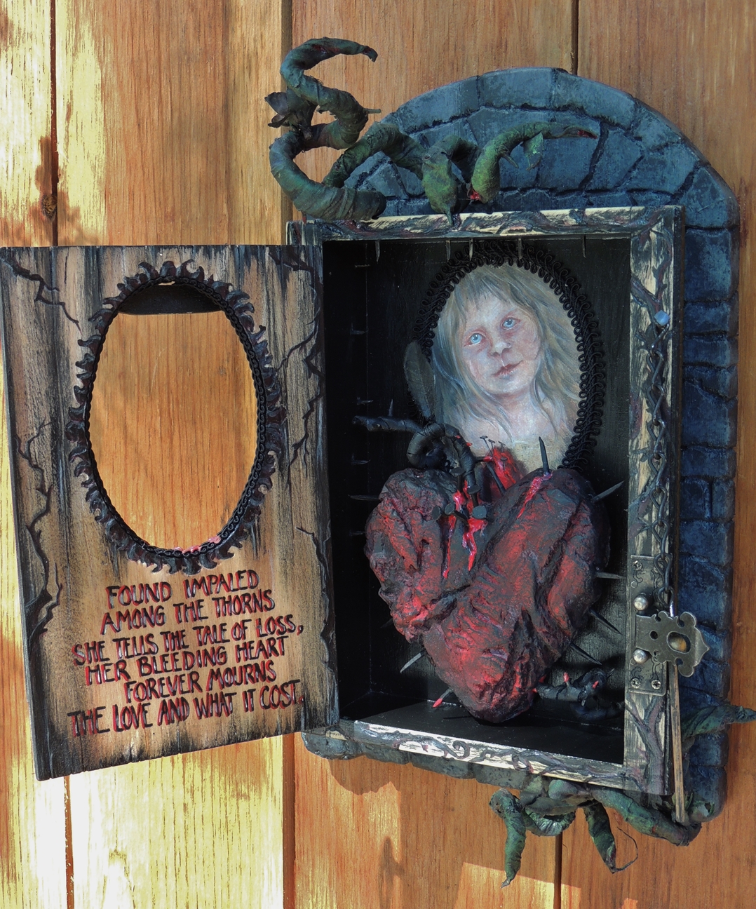 mixed media shadow box cabinet holding an impaled red heart with nails and a portrait of a pale poet hand painted poem on the door