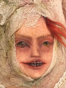 close up of a sinister face coming out of doll's belly red hair and metal teeth