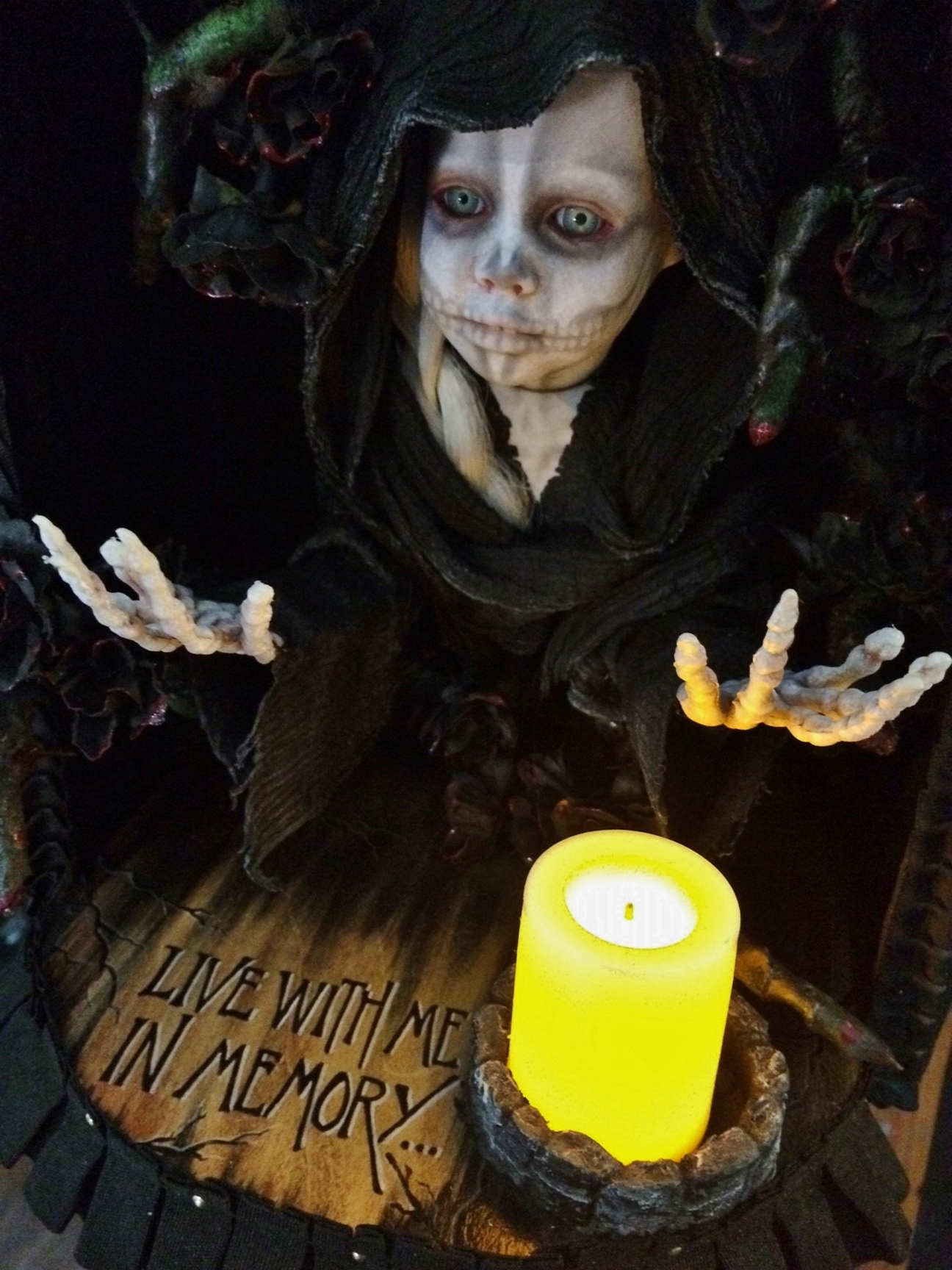 close-up mixed media altarbox and nightlight holding a saintly skeletal figure surrounded by black roses.