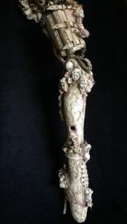 close-up art piece Prosthetic Leg adorned with porcelain doll heads, vintage textiles, lace & mixed media.