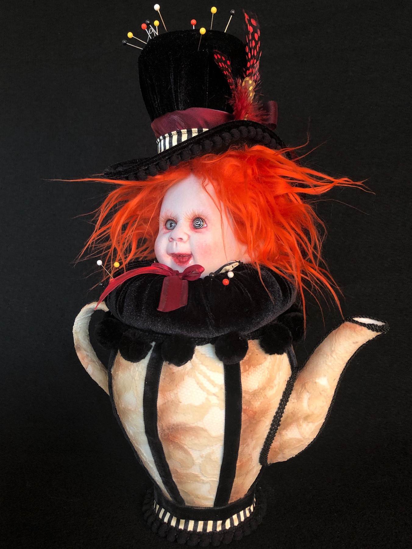 mad hatter themed pincushion porcelain doll head with bright orange hair and velvet tophat sits on a black velvet cushion set in lace-covered teapot