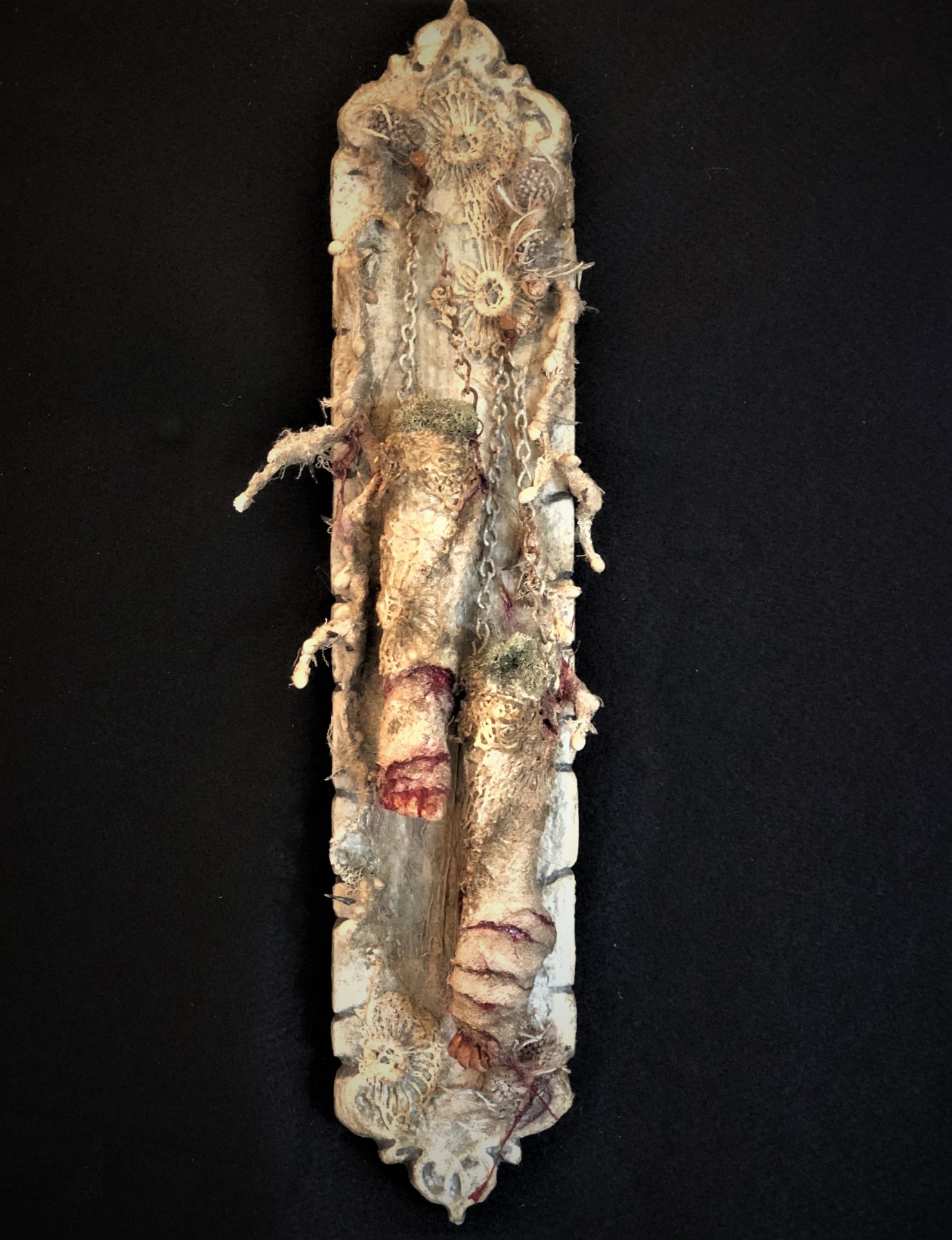 mixed media assemblage on board with severed feet held up by chain and hanging from nails