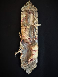 mixed media assemblage on board with severed, cracked and bleeding hands held up by chain and hanging from nails
