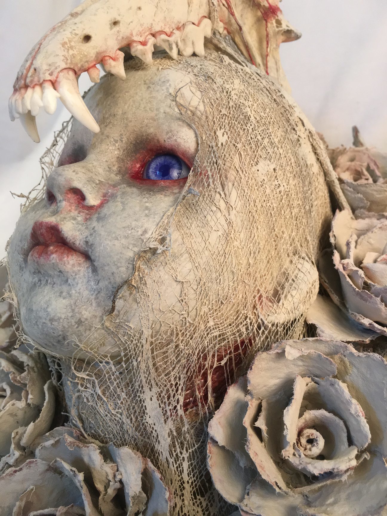 close up repainted baby doll head bone and white rose headdress red-rimmed blue eyes macabre