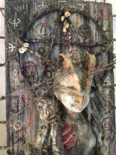 close-up mixed media assemblage plaque hand-painted babydoll with animal bones and pagan symbols