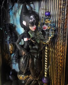 close up of mixed media assemblage shadow box diorama with a repainted goth doll staring into a mirror and ignoring her black eggs